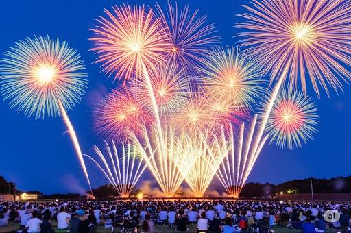 松戸花火大会 福祉と未来の展望をテーマとしたイメージでAIが生成した画像です。内容は都心での花火大会、打ち上げ花火とそれを見上げる松戸市民。