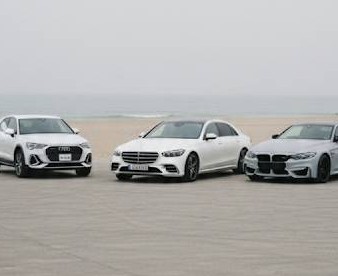 靄のかかった海辺の砂浜に、ドイツの高級車3台が駐車している。左側がアウディ、中央がベンツ、右側がBMWの画像です。