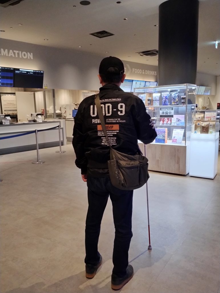 映画鑑賞が終わり、ユナイテッドシネマテラスモール松戸のフロアから男性の視覚障害者が帰宅する、後ろ姿の画像です。
