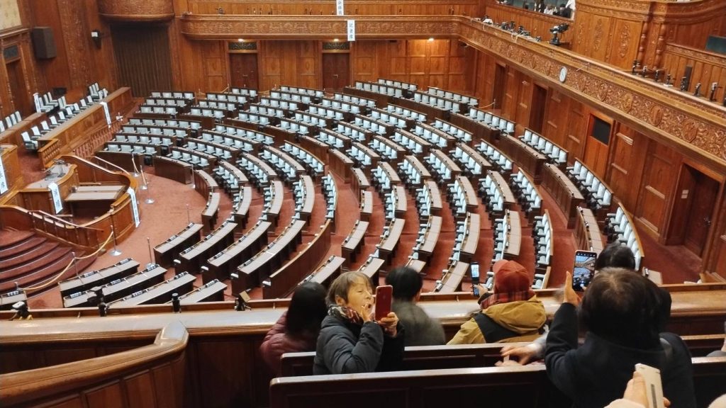 国会の議論をする場所を高い所から撮影した画像で、国会議員が座る席が扇状に並んでいます。
