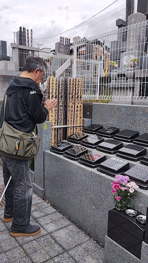 常真寺母の墓参りに行った時の画像です。お墓に向かって男性視覚障害者が手を合わせてお参りをしています。