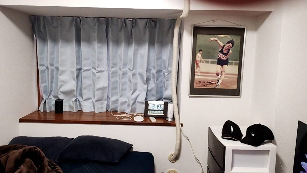 5.5畳の洋室の部屋にある水色のハーフカーテンと、槍投げ選手のパネル写真の画像です。
