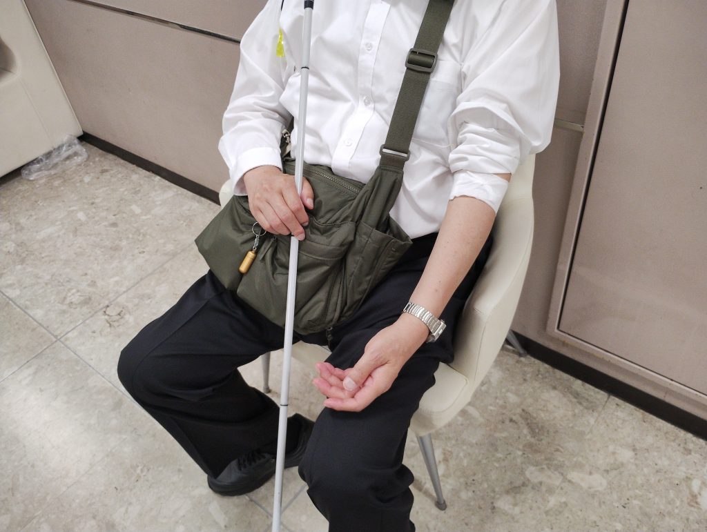 献血をした後に止血の為、絆創膏の上に包帯を一時的に腕に巻いた視覚障害者男性の座っている画像です。